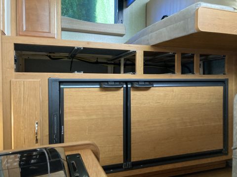 2015 Ford F-550 - This is an interior shot of a recreational vehicle showing wooden cabinetry, a refrigerator with two doors, and the underside of a bed.