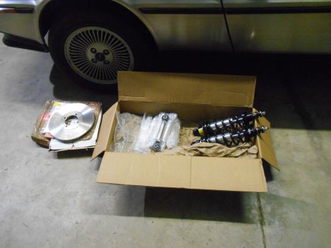 1992 Ford Bronco - A cardboard box containing car parts, including two shock absorbers and a brake rotor, sits on a concrete floor next to the wheel of a silv…
