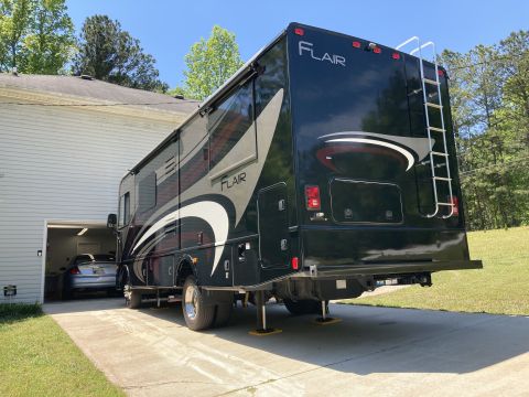 2015 Ford F-550 - The rear and side of a black Fleetwood Flair motorhome parked on a concrete driveway next to a house and garage. The motorhome has a ladder…