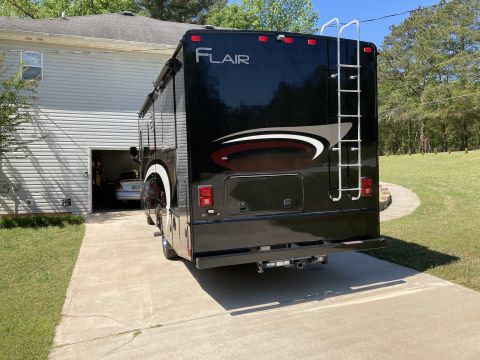 2015 Ford F-550 - The rear of a black Fleetwood Flair motorhome is parked on a concrete driveway next to a residential garage. A silver car is visible inside…