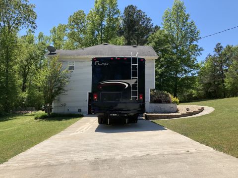 2015 Ford F-550 - The rear of a black Fleetwood Flair RV is parked on a concrete driveway in front of a light blue house. The RV has a ladder on the back and…