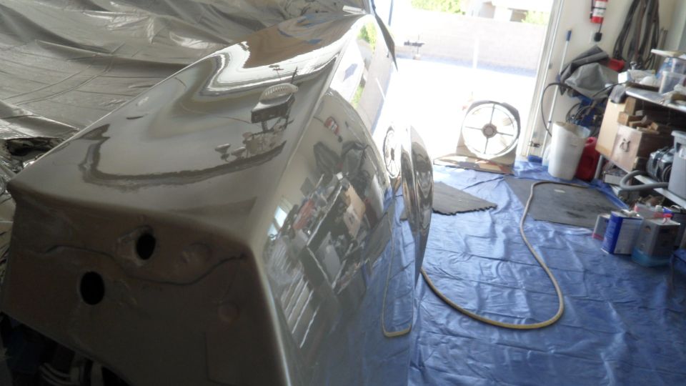 Gray primed vehicle rear quarter panel with plastic sheeting, reflecting garage interior.