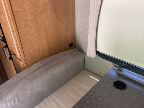 2015 Ford F-550 - An interior view shows a built-in bench seat with grey upholstery next to a wooden cabinet and a window with a cream-colored roller shade.