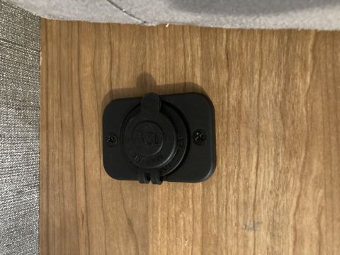 2015 Ford F-550 - A black 12V marine socket is mounted on a light wood-grain surface. The socket has a cap and is secured with two black screws.