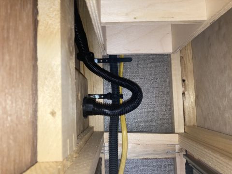2015 Ford F-550 - A close-up view of black corrugated tubing and a yellow wire secured with black zip ties and metal brackets to wooden framing. The backgrou…