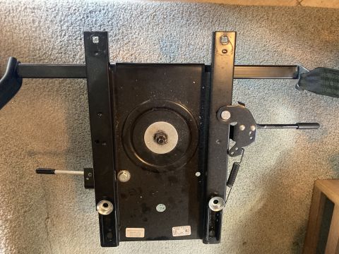 2015 Ford F-550 - A black metal seat swivel mechanism with a lever on the right side is shown from a top-down perspective, resting on a carpeted floor.