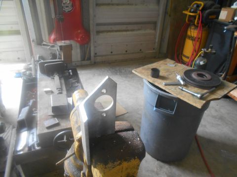 1992 Ford Bronco - A metal bracket with two holes and a large circular cutout is clamped in a yellow vise. In the background, a large gray trash can is topped…