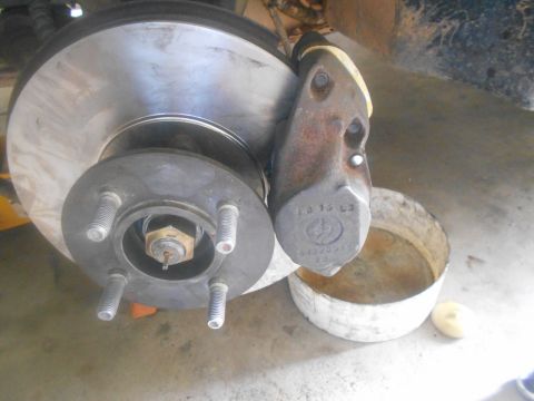 1992 Ford Bronco - A close-up view of a vehicle's brake rotor and caliper assembly, showing the lug nuts and part numbers on the caliper. A white cylindrical…
