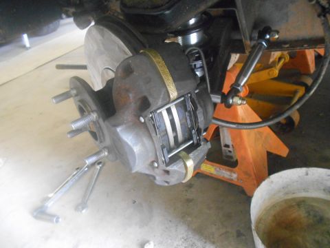 1992 Ford Bronco - A close-up view shows a vehicle's brake caliper and rotor assembly, supported by an orange jack stand. Tools, including a socket wrench and…