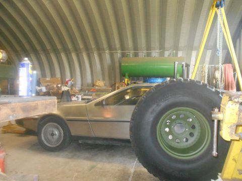 1992 Ford Bronco - A side view of a DeLorean DMC-12 with a large tire in the foreground, inside a corrugated metal building.