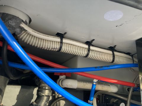 2015 Ford F-550 - Corrugated tubing secured with zip ties to the underside of a vehicle, with blue and red PEX tubing visible below.