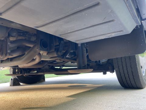 2015 Ford F-550 - Undercarriage view of a large vehicle, likely an RV or truck, showing the exhaust system, suspension components, and a rear tire. The vehic…
