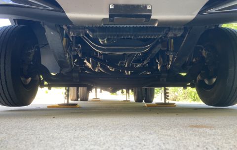 2015 Ford F-550 - Undercarriage view of a large truck or RV, showing the suspension, dual rear wheels, and yellow stabilizing jacks on the ground.