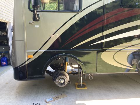 2015 Ford F-550 - The front passenger side of a large RV is shown with the front wheel removed and the chassis supported by a jack. The RV has a tan and dark…