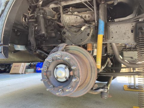 2015 Ford F-550 - A close-up, low-angle view of the front driver's side suspension and braking system of a large truck, likely undergoing maintenance. The br…