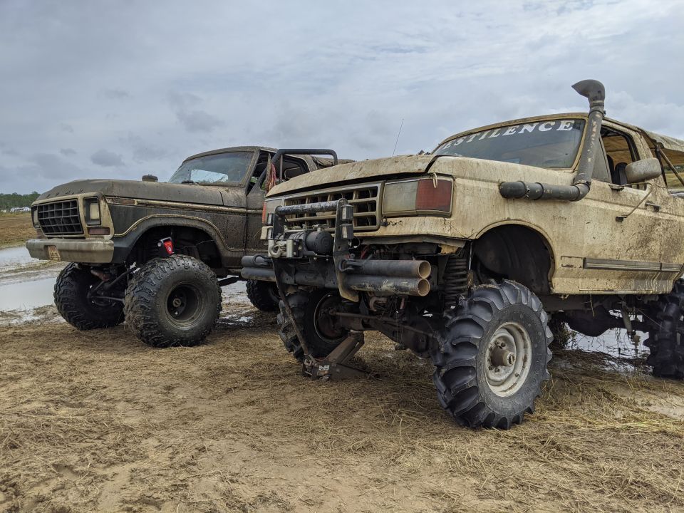 Two mud-covered Ford Broncos with large off-road tires parked in a muddy field.