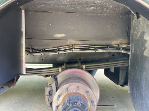 2015 Ford F-550 - The underside of a vehicle shows a large brake rotor and caliper assembly, with leaf springs supporting the chassis. Bundles of wiring are…