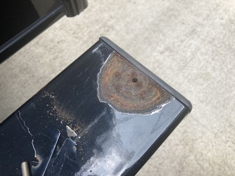 2015 Ford F-550 - A close-up view of a black metal part with significant rust and peeling paint on the corner. The part appears to be a component of a vehicl…