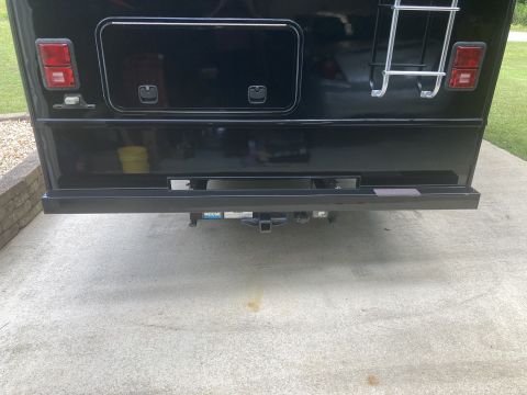 2015 Ford F-550 - The rear of a black RV is shown, featuring taillights, storage compartments, a ladder, and a trailer hitch with a Reese hitch receiver.