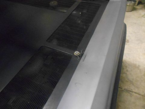 1992 Ford Bronco - A close-up, high-angle view of the hood of a vehicle, showing a black textured grille section and a gray fender. A bolt with a washer is vi…