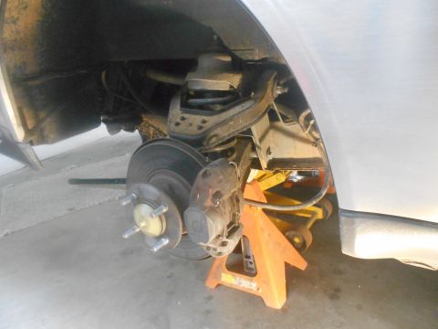 1992 Ford Bronco - A close-up view of the front passenger-side wheel assembly of a vehicle, supported by an orange jack stand. The brake rotor, caliper, and h…