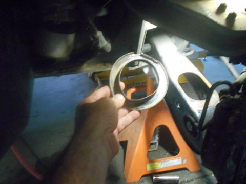 1992 Ford Bronco - A hand holds a metal ring, likely a spacer or gasket, in front of a vehicle's suspension components supported by an orange jack stand.