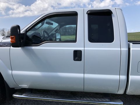 2011 Ford F-250 - The side view of a white Ford F-250 pickup truck shows the front passenger door, rear door, and side mirror. A chrome step bar runs along t…
