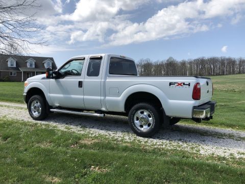 2011 Ford F-250 - A white Ford F-250 Super Duty pickup truck is parked on a gravel driveway in front of a house with a wooded area in the background. The tru…
