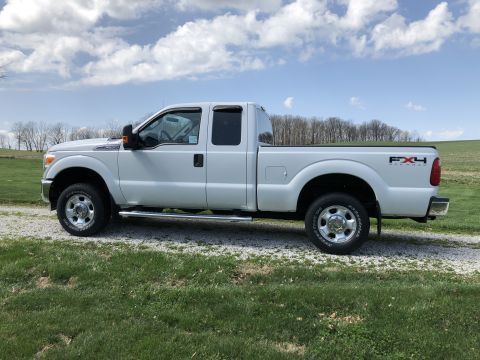 2011 Ford F-250 - A white Ford F-250 Super Duty pickup truck is parked on a gravel driveway next to a grassy field under a partly cloudy sky. The side view s…
