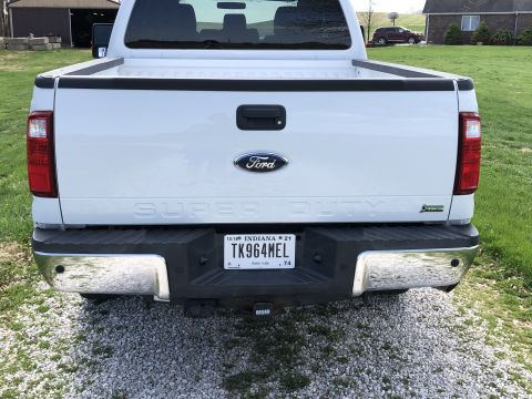 2011 Ford F-250 - The rear of a white Ford F-250 Super Duty pickup truck is shown parked on a gravel driveway with grass on either side. The truck has a chro…