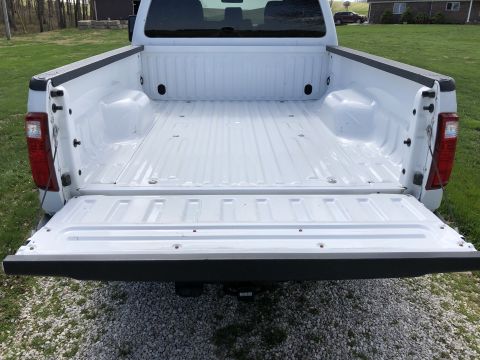 2011 Ford F-250 - The open tailgate of a white Ford F-250 pickup truck is shown from a rear-facing perspective. The truck bed is clean and empty, with a grav…