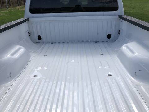 2011 Ford F-250 - The empty white bed of a pickup truck is shown from a rear-facing angle. The ribbed metal floor of the truck bed is visible, along with tie…