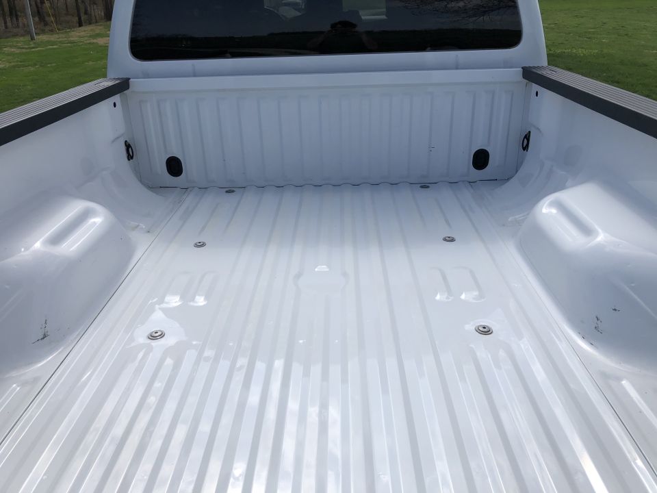 Empty white pickup truck bed with ribbed floor and visible tie-down points.