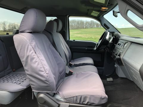 2011 Ford F-250 - The interior of a Ford F-250 pickup truck shows the front passenger and driver seats covered in gray seat covers. The dashboard and steerin…