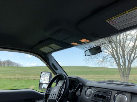 2011 Ford F-250 - Interior view of a pickup truck, looking out the windshield at a grassy field and trees under a partly cloudy sky. The dashboard, steering…