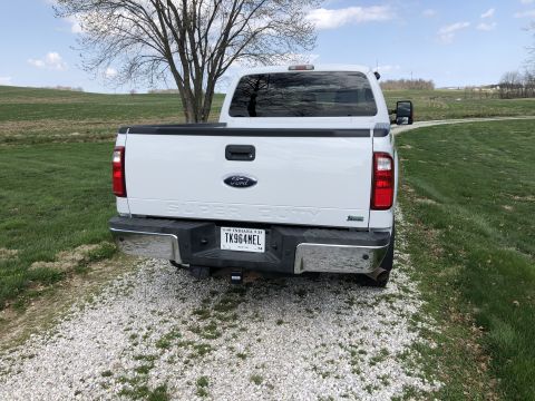 2011 Ford F-250 - The rear view of a white Ford Super Duty pickup truck parked on a gravel driveway next to a grassy field. The truck has a chrome bumper and…