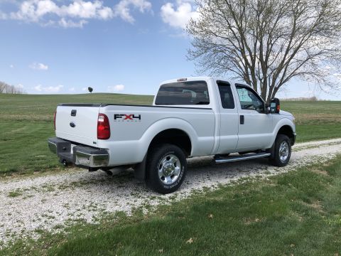 2011 Ford F-250 - A white Ford F-250 Super Duty pickup truck is parked on a gravel driveway next to a grassy field and a large tree. The truck is viewed from…