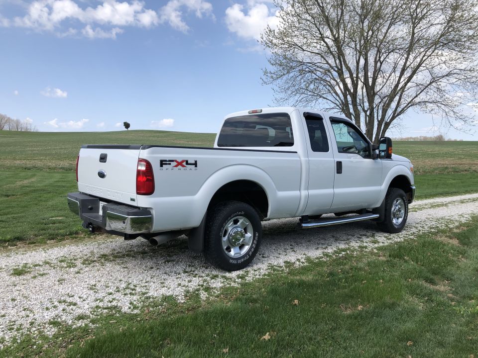 White Ford F-250 Super Duty pickup truck parked on a gravel driveway with a large tree and grassy field.