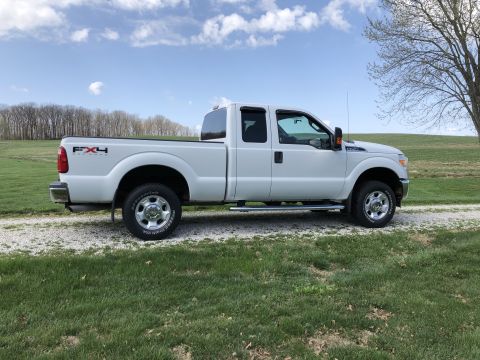 2011 Ford F-250 - A white Ford F-250 Super Duty pickup truck is parked on a gravel driveway with a grassy field and trees in the background under a partly cl…