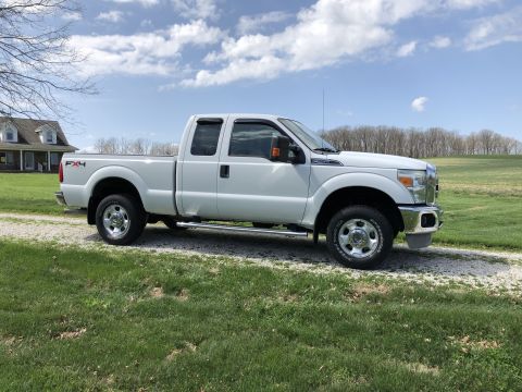 2011 Ford F-250 - A white Ford F-250 Super Duty pickup truck is parked on a gravel driveway next to a grassy lawn. The truck is shown from the side profile w…