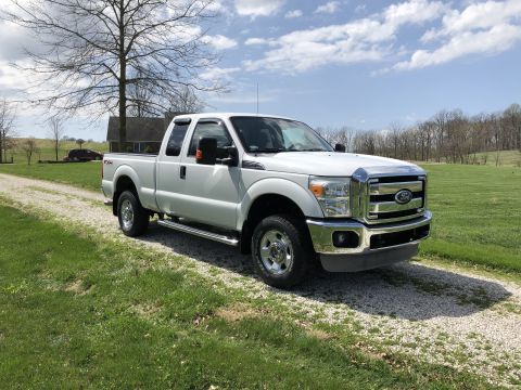 2011 Ford F-250 - A white Ford F-250 Super Duty pickup truck is parked on a gravel driveway in front of a house with trees in the background.