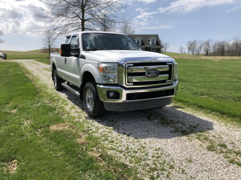 2011 Ford F-250 - A white Ford F-250 pickup truck is parked on a gravel driveway in front of a grassy field and a house. The truck is viewed from a 3/4 front…