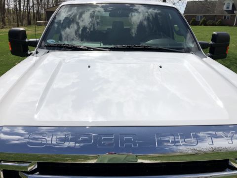 2011 Ford F-250 - The front view of a white Ford Super Duty pickup truck is shown, focusing on the hood and grille. The chrome grille has the words "SUPER DU…