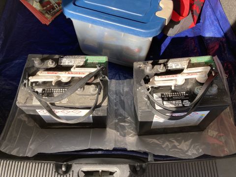 2015 Ford F-550 - Two automotive batteries are shown in the back of a vehicle, resting on a blue tarp and covered with plastic sheeting. The batteries appear…