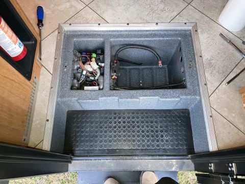 2015 Ford F-550 - A view looking down into an open compartment containing electrical components, fuses, and wiring, with a black rubber mat in the foreground.