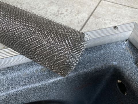 2015 Ford F-550 - A roll of fine metal mesh screen is placed over the edge of a gray textured surface, possibly a vent or filter housing, within an aluminum…