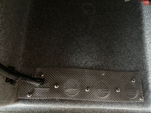 2015 Ford F-550 - A close-up view shows a metal mesh screen secured with screws to a dark gray carpeted surface. A black corrugated conduit is attached to th…