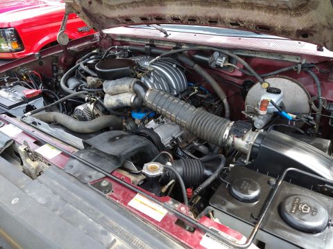 1996 Ford Bronco - The engine bay of a maroon vehicle is shown, with a red vehicle visible in the background.