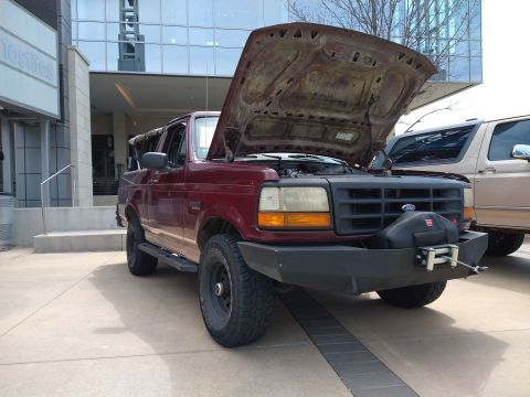 1996 Ford Bronco - Maroon 1996 Ford Bronco with hood open, parked outside a modern building.
