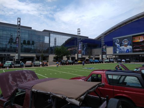 1996 Ford Bronco - A line of Ford Broncos and other vehicles are parked on a football field outside a stadium.